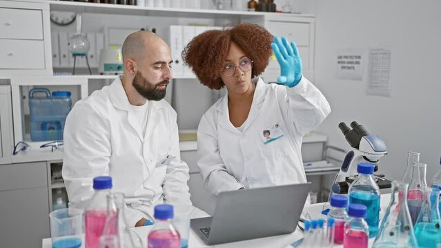 Two serious scientists speaking together, discovering research insights on laptop at indoor lab