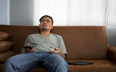 Asian young upset depressed man sitting alone in living room at home. Attractive unhappy male...