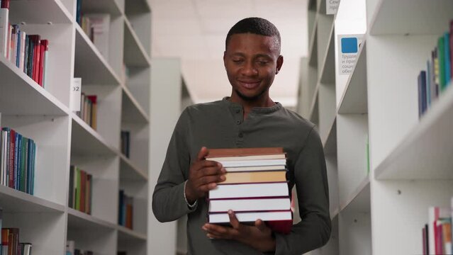 Positive teacher holds books in school library. African American student prepares literature stack to do homework in bookstore. Black guy with folios