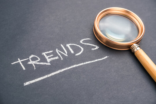 TRENDS word handwriting with chalk, and magnifying glass, on black paper, trend analysis