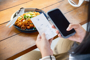 Closeup woman is holding a food receipt and smart phone in the restaurant, scan, or online payment,...