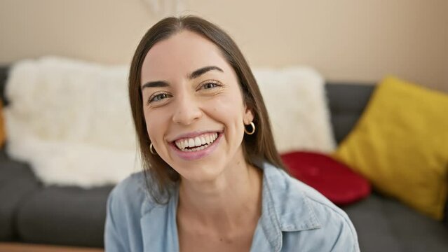 Cheerful portrait of a confident young hispanic woman joyfully sticking her tongue out while relaxing on her indoor home sofa.
