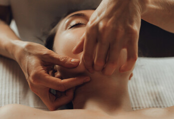 Hands of female chiropractor massaging face of young woman lying on massage table. Visceral...