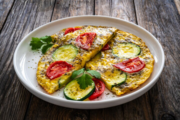 Omelette - scrambled eggs with mozzarella cheese, zucchini and tomatoes on wooden table
