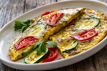 Omelette - scrambled eggs with mozzarella cheese, zucchini and tomatoes on wooden table
