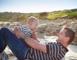 Young father playing with baby son as lying at the beach, smiling happy having fun