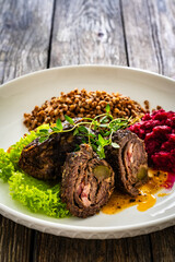 Wrapped beef in sauce served with boiled buckwheat and grated beets on wooden table
