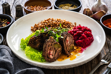 Wrapped beef in sauce served with boiled buckwheat and grated beets on wooden table
