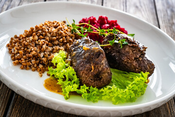Wrapped beef in sauce served with boiled buckwheat and grated beets on wooden table
