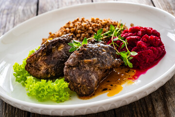 Wrapped beef in sauce served with boiled buckwheat and grated beets on wooden table
