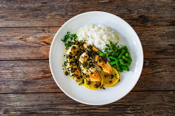 Chicken piccata with white rice and capers in sauce on wooden background 