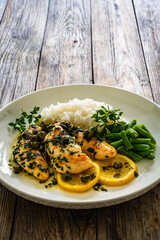 Chicken piccata with white rice and capers in sauce on wooden background
