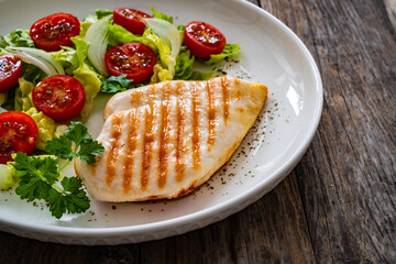 Grilled chicken breast and fresh vegetables on wooden table
