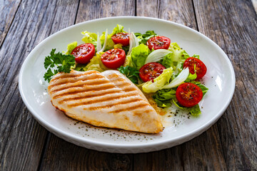 Grilled chicken breast and fresh vegetables on wooden table
