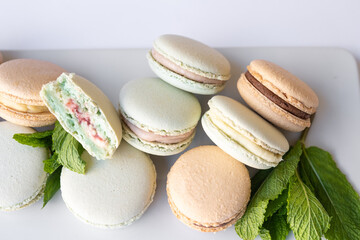 Macaroons of different colors with sprigs of mint on a white background.