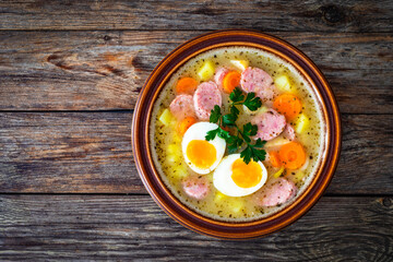  Sour rye soup with sausages and boiled eggs on wooden table