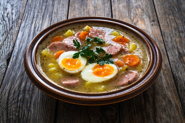  Sour rye soup with sausages and boiled eggs on wooden table