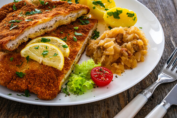 Crispy breaded fried cutlet with boiled potatoes and cooked cabbage on wooden table
