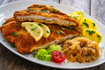 Crispy breaded fried cutlet with boiled potatoes and cooked cabbage on wooden table

