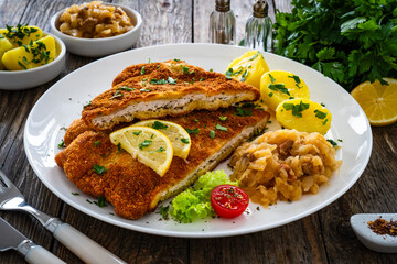 Crispy breaded fried cutlet with boiled potatoes and cooked cabbage on wooden table
