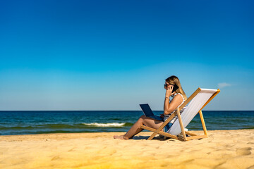 Mid adult woman using laptop and smartphone on beach
