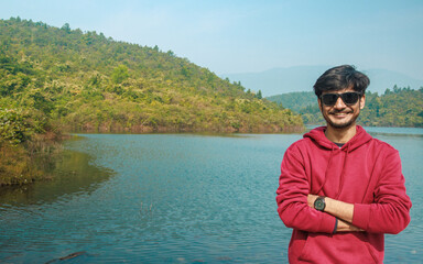 Handsome man wearing sunglasses on winter vacation day - Happy hiker with smiling at camera outside - Tourist walking near the mountain and lake - Traveling and tourism concept. 