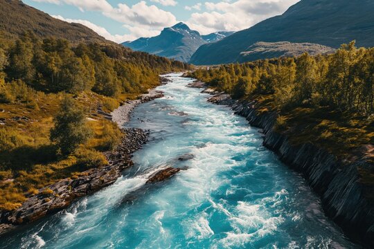 Drone high-angle photo of the turquoise-colored mountain river flowing in the pine woodland with a view of the mountain peaks in the background in Innlandet County, Norway 