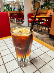 Delicious cold coffee drink. Fresh cocktail with ice and lemon slices and straws. Cold cappuccino is on white checkered table.