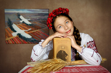 The girl is dressed in Ukrainian clothes, a vyshyvanka, a wreath, with the book Kobzar by Taras Shevchenko - obrazy, fototapety, plakaty