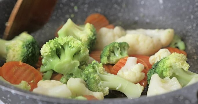 Cooking and stirring frozen vegetables in a frying pan