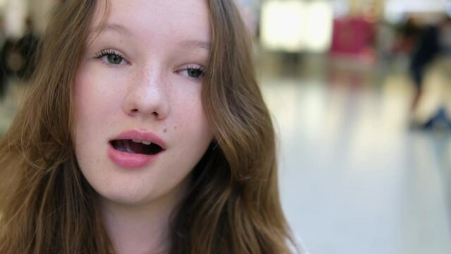 teenage girl, smile, upset, lower eyes, look to side, show heart, squint nose, look out with eyes send kiss. beautiful people Real life against background of walking people adolescence woman