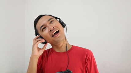 happy face of young asian man with headphone listening and enjoying music, podcast, video or radio from smartphone