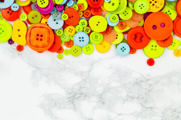 Scattered colorful buttons on white table. Pile of multicolored buttons on one side of the picture. Copy space. Good for logos of sewing or tailoring work. Home needlework. Flat lay banner with button