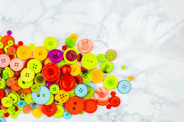 Scattered colorful buttons on white table. Pile of multicolored buttons on one side of the picture. Copy space. Good for logos of sewing or tailoring work. Home needlework. Flat lay banner with button