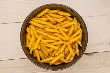 Raw pasta, penne, in a ceramic plate on a wooden table, macro, top view.