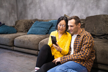 Young couple using smartphone while sitting on floor in living room at home