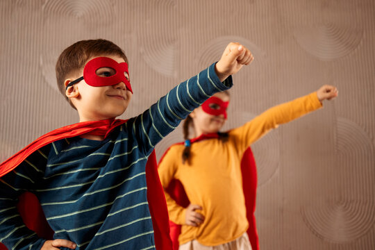 Portrait of a team of two young superheroes, brother and sister, over beige background