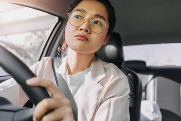 Front view of asian Thai woman wear eye glasses, driving car alone on road while going to work in the morning.