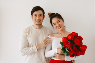 Happy Asian couples holding red roses, both woman and man smiling to camera, enjoy good time together on Valentines, isolated over white wall.