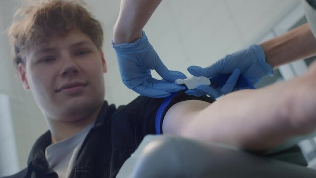 Lab assistant applying tourniquet on young man patient arm before taking venous blood for test or intravenous injection. Collecting blood from a teenager. Laboratory in clinic or hospital for donation
