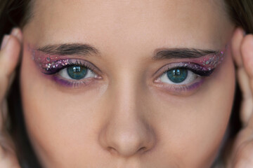 Cropped shot of a young caucasian woman with purple and pink eye shadow and glitter on the eyelids. Festive makeup. Party, holiday concept. Close up - Powered by Adobe