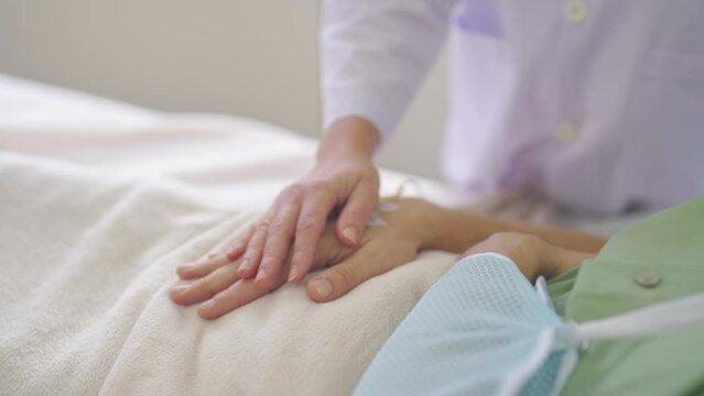 Close up hands of doctor hold patient hand to encourage or hearten to fight with the disease and patient lie on bed in hospital.