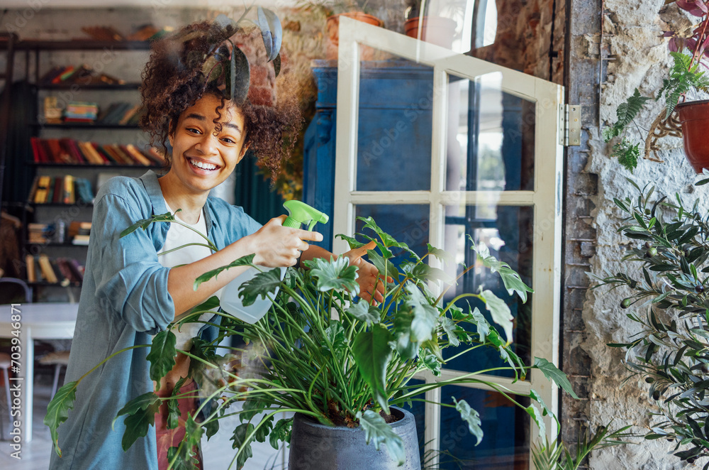 Wall mural Young Afro American woman plant lover taking care of houseplant