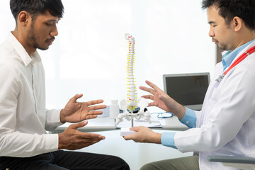 Doctor or physical therapist points to human skeleton on lower back to guide and consult male...