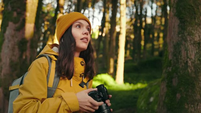 A young woman in a warm jacket and yellow hat explores the forest, capturing moments with her professional camera