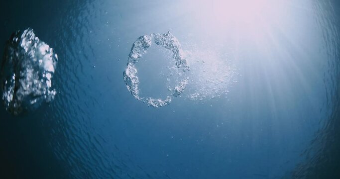 Underwater ring bubbles made by diver and sun light in clear blue ocean.