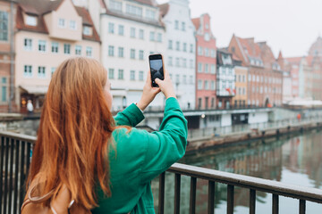 Back view of young European tourist makes photo or video on smartphone at city of Gdansk, Poland....