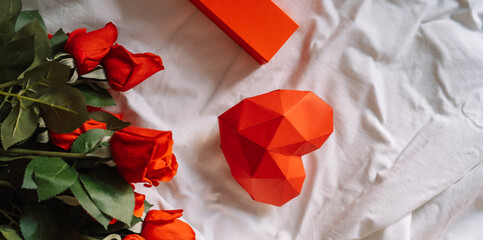 Paper red heart with a gift and a bouquet of roses on a white bed