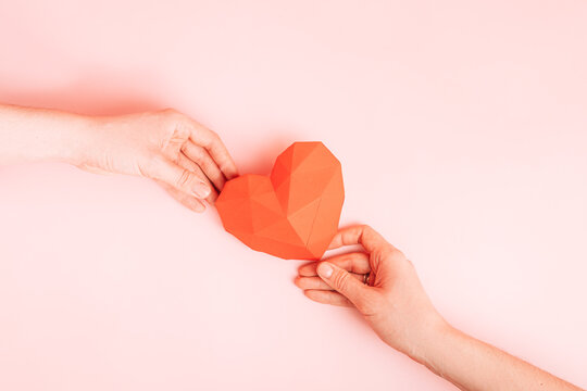 Passing a red paper heart from one hand to another on a pink background.