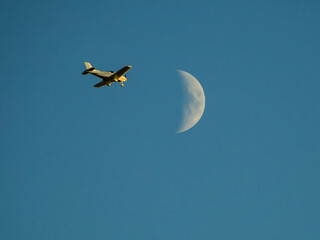 Sunlit flying airplane and moon in blue sky
